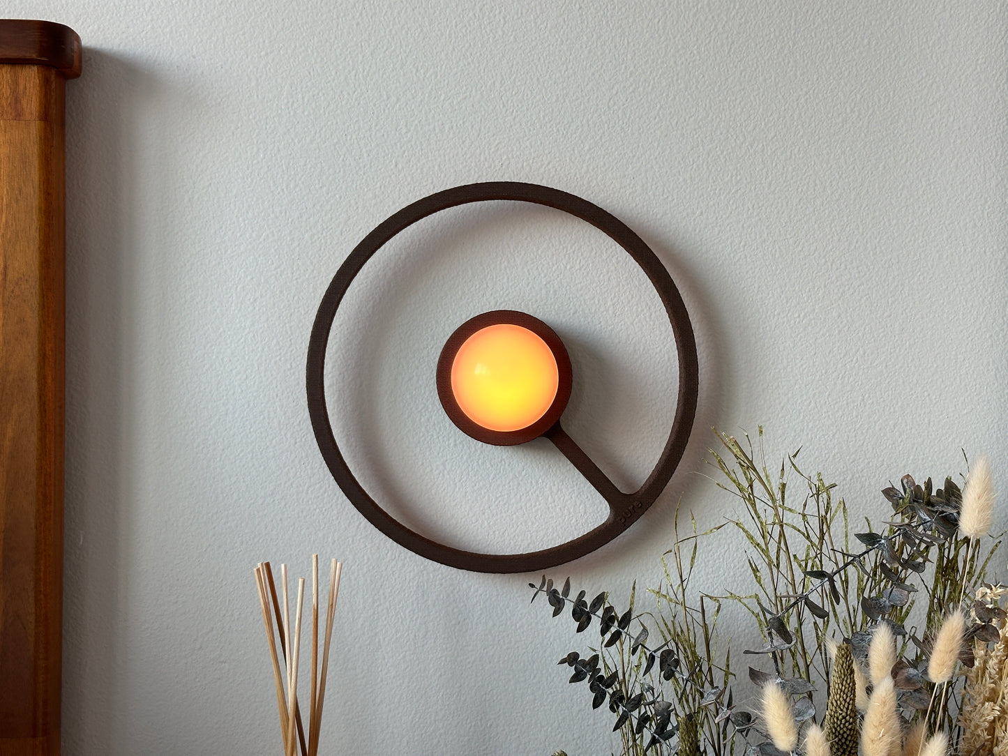 Pure MDRN ORA sconce in Coffee color on a bedroom wall next to a bed.