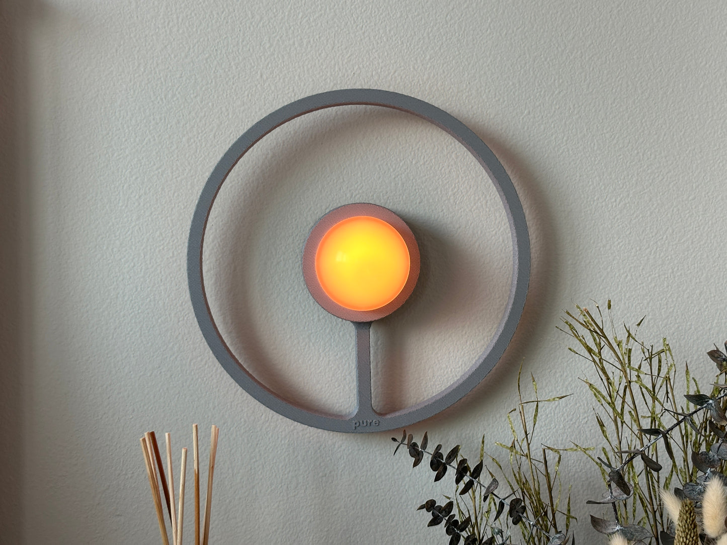 Pure MDRN ORA sconce in Ash color on a bedroom wall next to a bed.