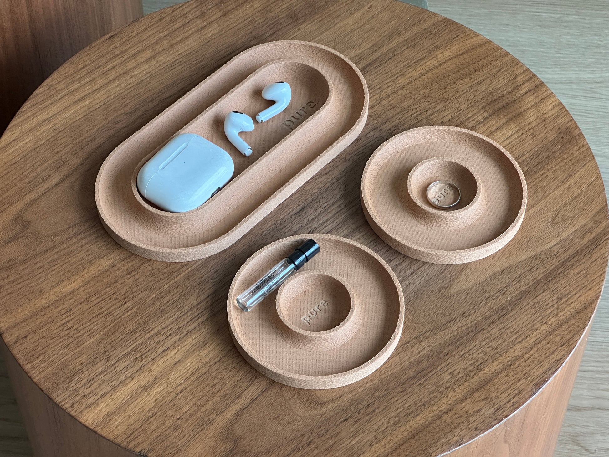 Three-piece valet tray set in earthy modern colors, including one long tray and two round catchall trays on a wood table.