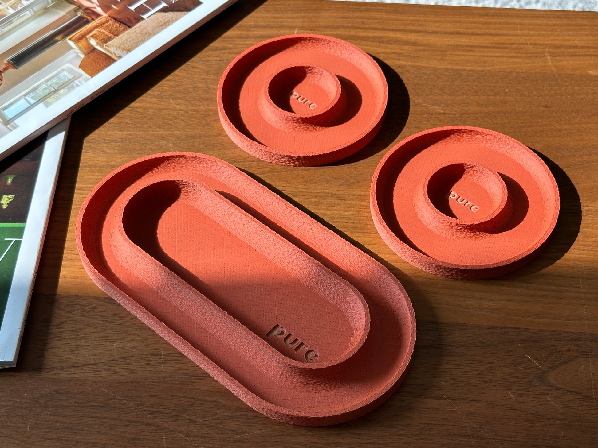 Terracotta valet tray set with one long tray and two round trays on a wood table.