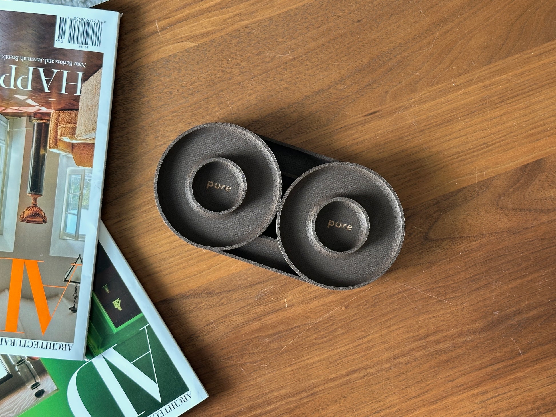 Chocolate brown pair of round catchall trays styled beside design magazines on a wood table.