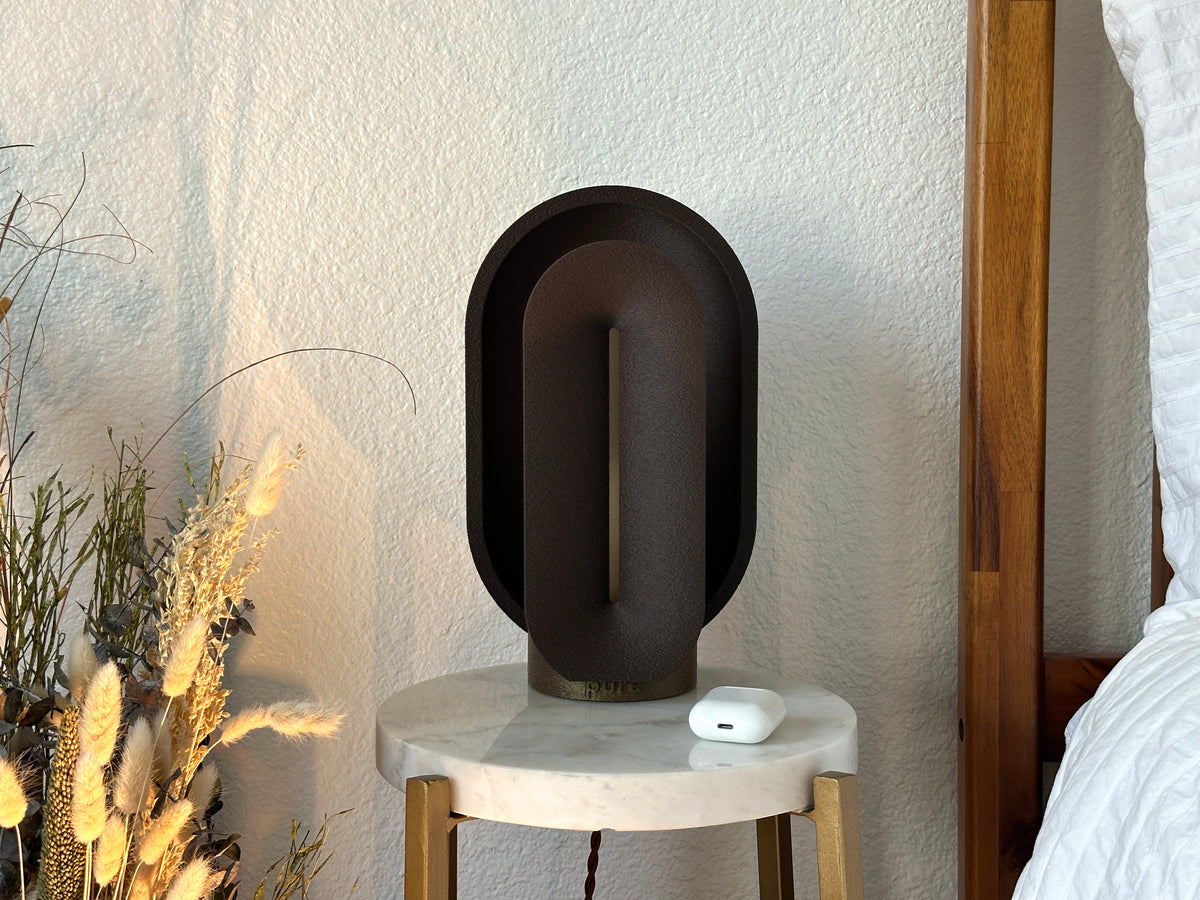 Turned off coffee brown statement lamp on a marble table, showing its matte textured finish and clean mid century modern silhouette.