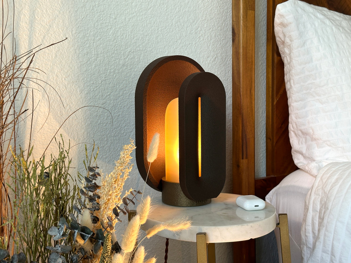 Angled view of the coffee brown sculptural lamp beside white bedding, showing the layered body and translucent amber light shield.