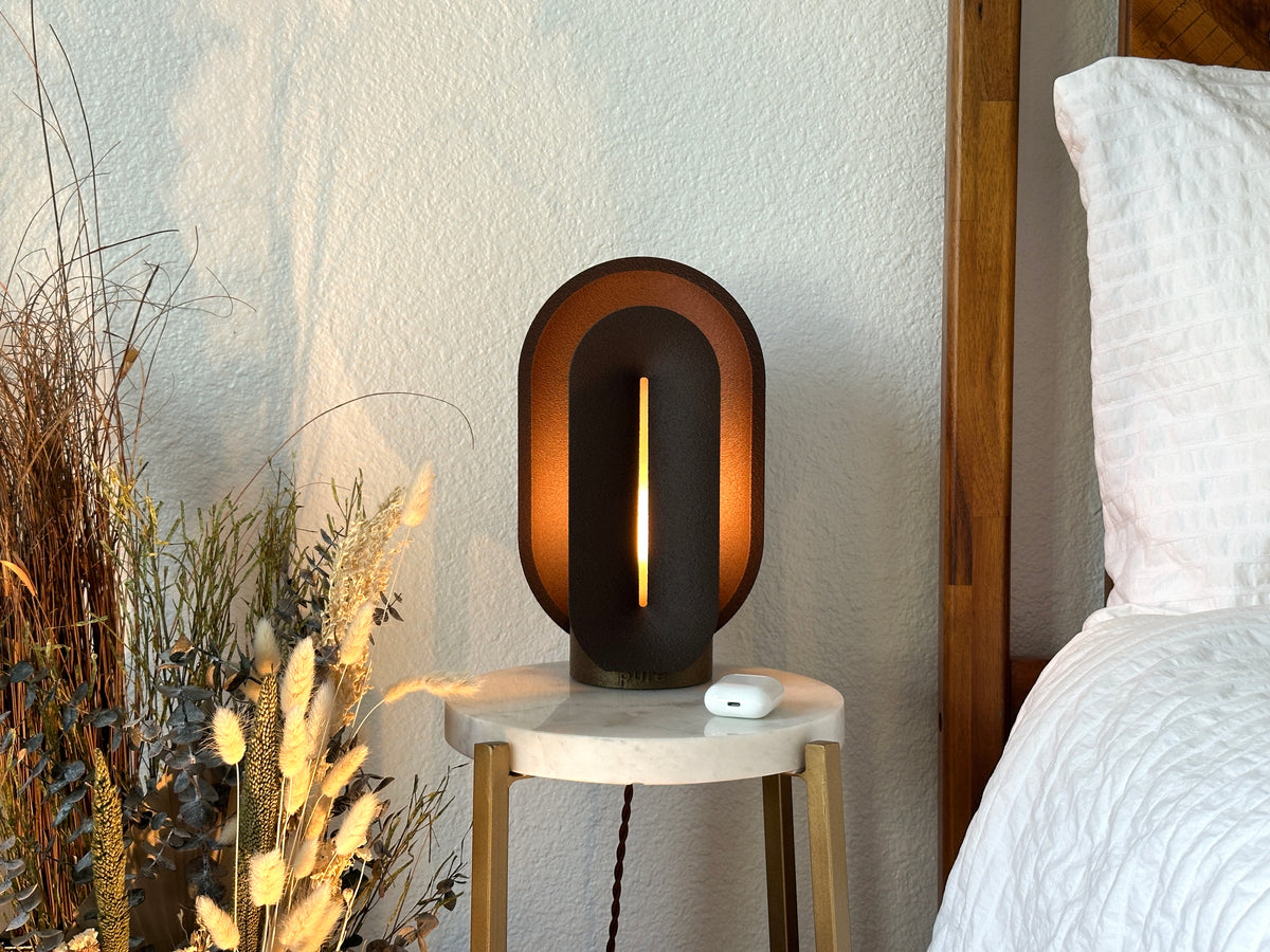 Coffee brown table lamp glowing on a marble bedside table beside a wood bed, styled as a warm mid century modern bedroom scene.