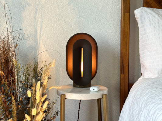 Coffee brown table lamp glowing on a marble bedside table beside a wood bed, styled as a warm mid century modern bedroom scene.