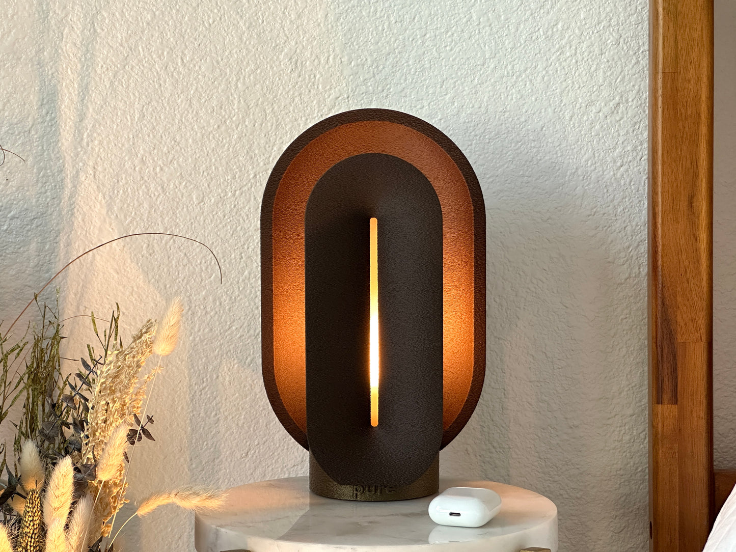 Front view of the coffee brown mid century lamp illuminated on a marble side table, showing its sculptural shape and warm amber glow.