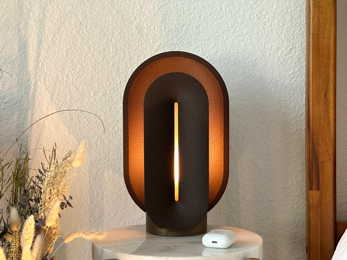 Front view of the coffee brown mid century lamp illuminated on a marble side table, showing its sculptural shape and warm amber glow.