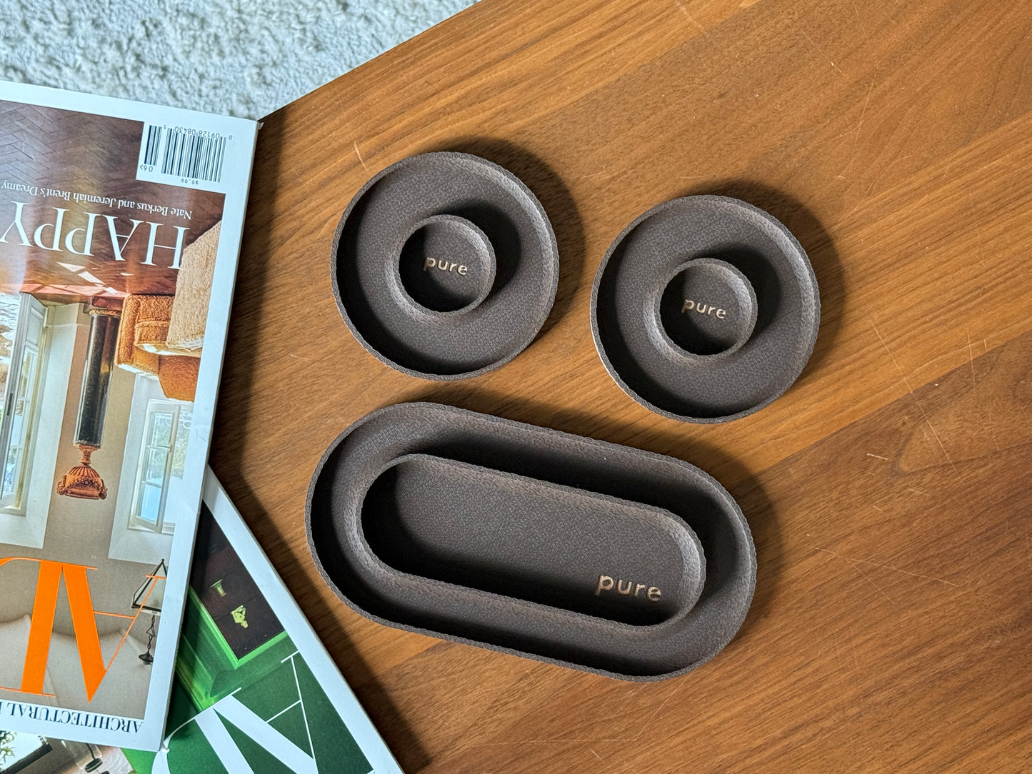 Dark brown valet tray set with one long tray and two round catchall dishes beside a magazine.