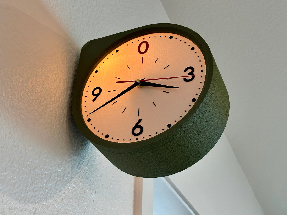 Angled view of a Moss Green double sided wall clock with warm backlit face, showing the depth of the retro station clock design.