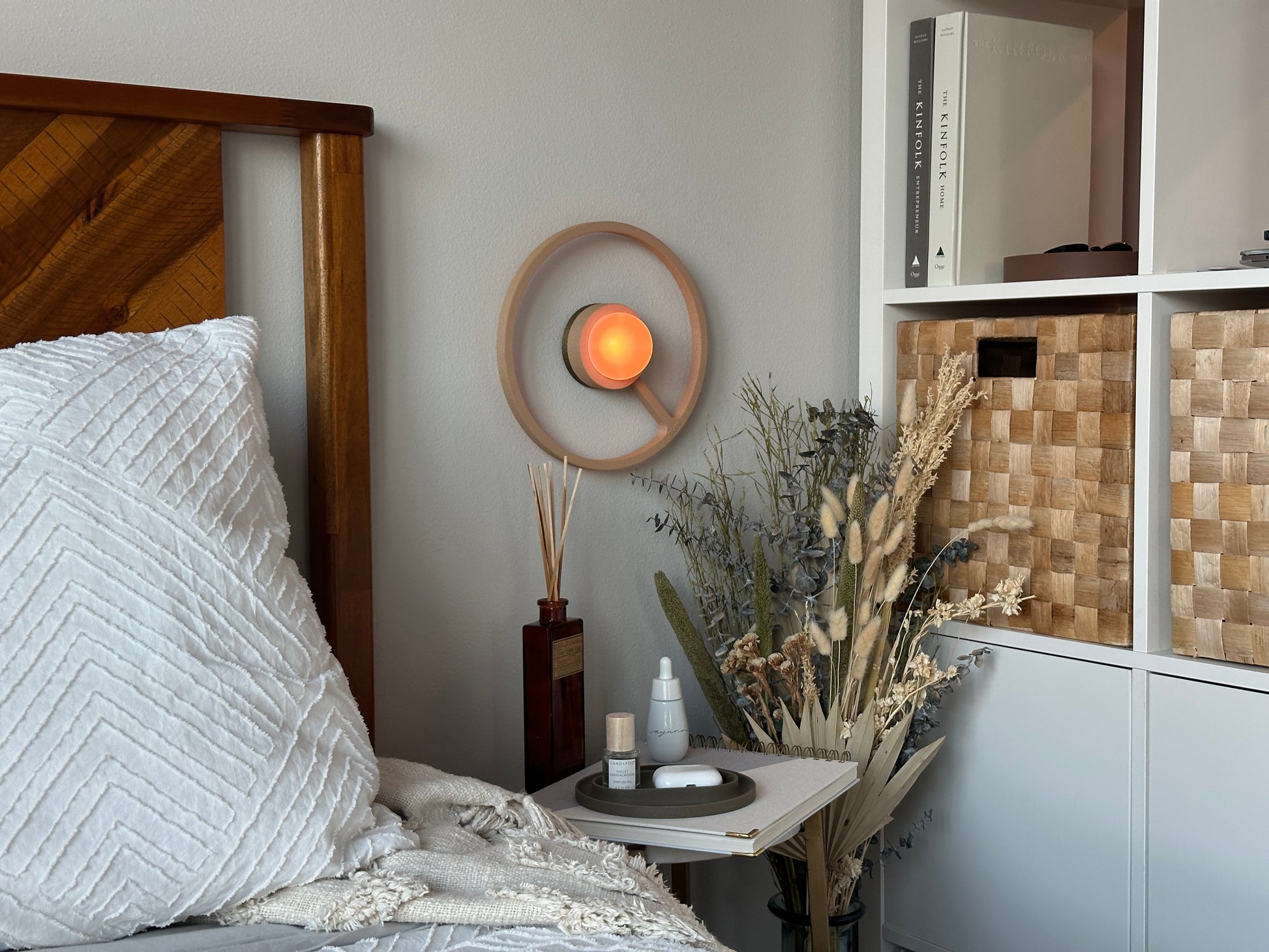 Cozy bedroom with wooden headboard, white bedding, and decorative elements. Pure MDRN ORA sconce in Sand color on a bedroom wall next to a bed.