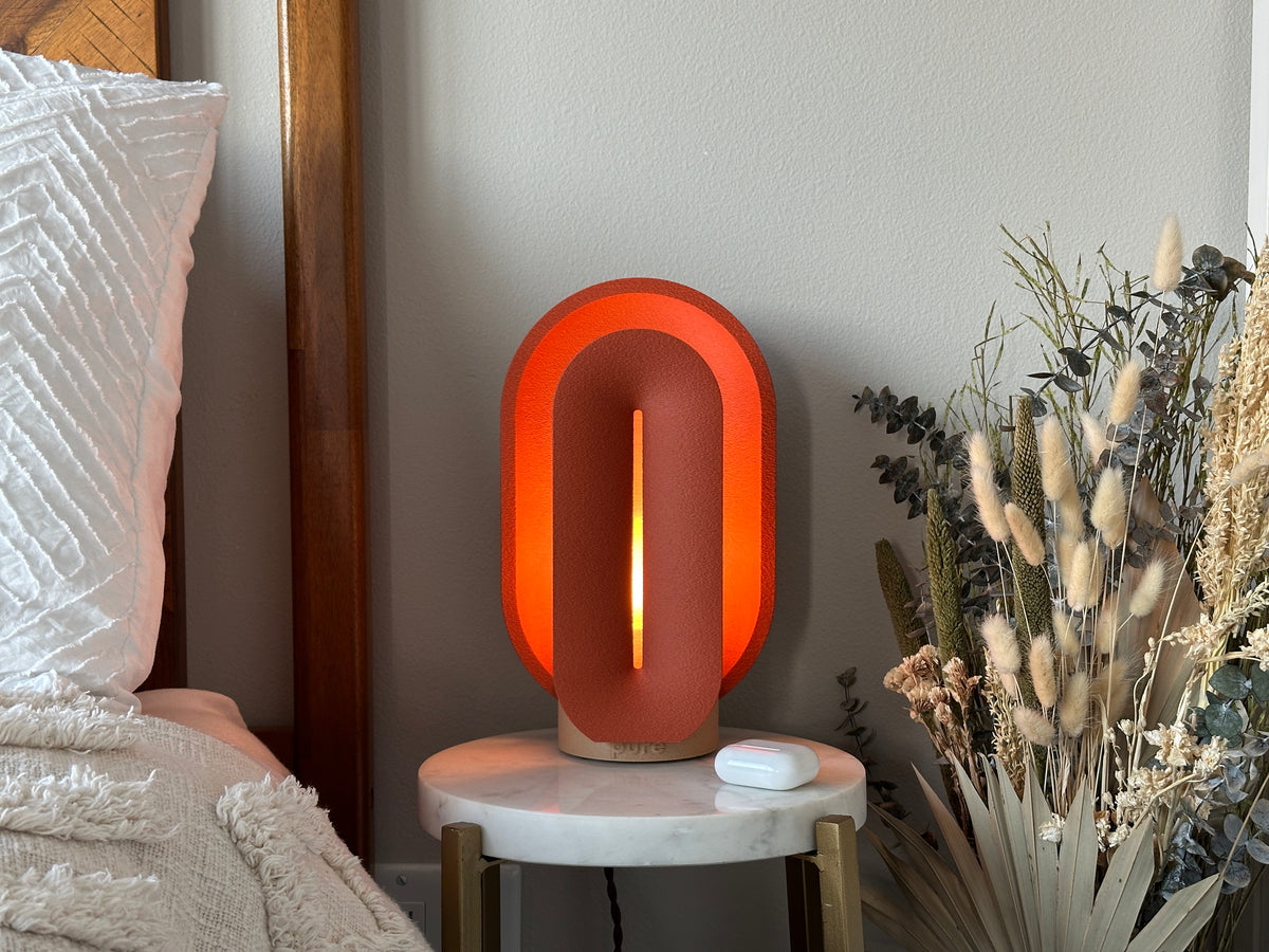 Terracotta small table lamp glowing beside a wood bed frame, white bedding, and dried flowers on a marble nightstand.